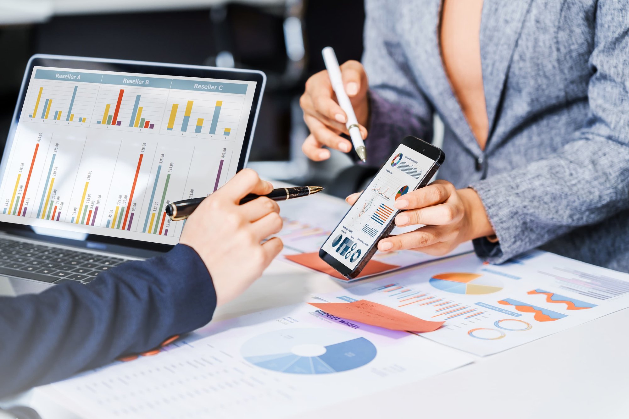 two community corrections employees are comparing county data by looking at charts on their phones, their laptops, and on printouts.