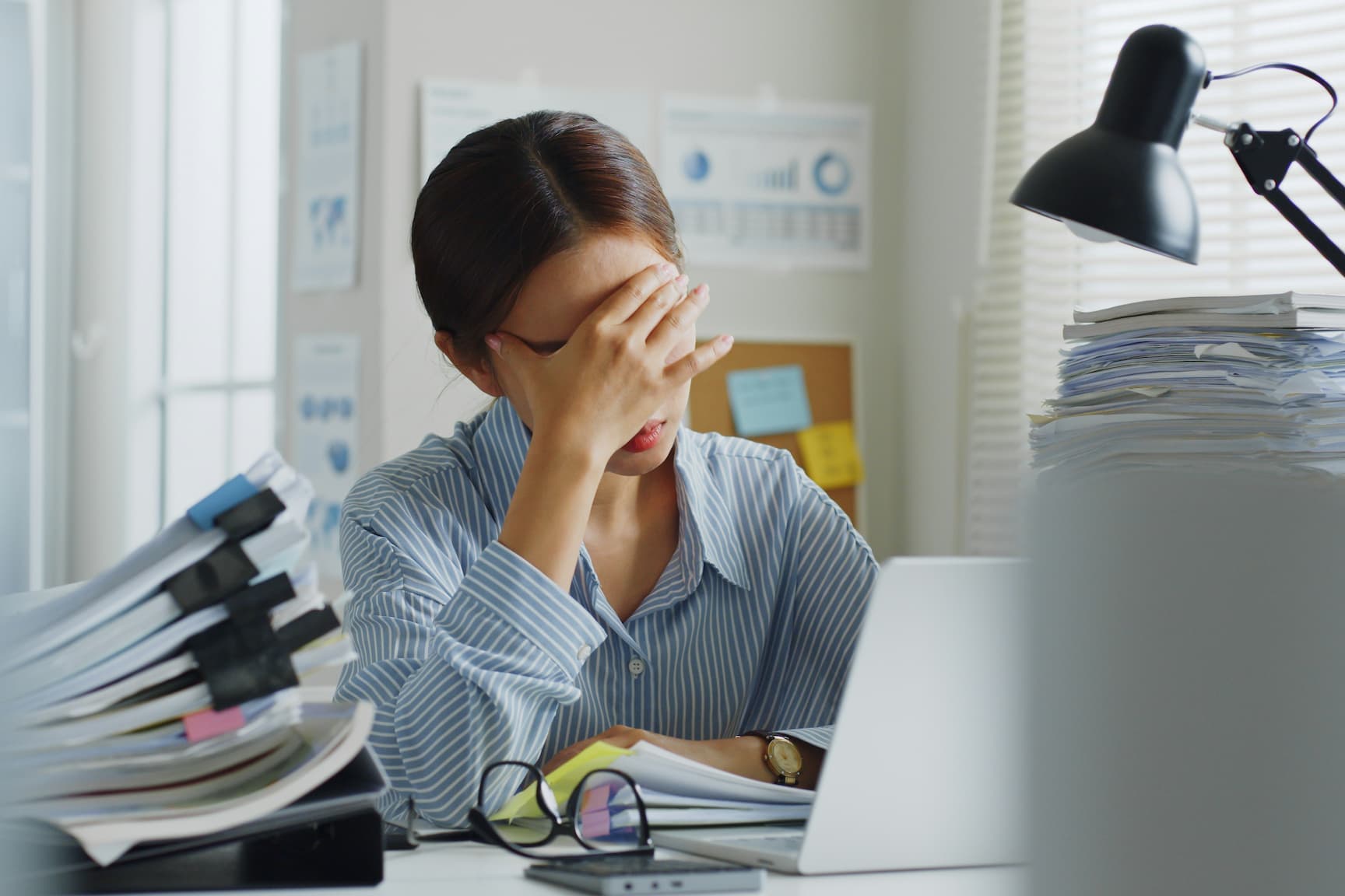 a frustrated employee holding their face while looking at computer screen, representing being annoyed with manual reporting process.